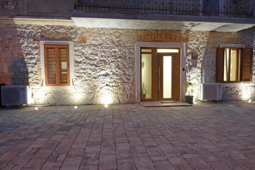 Stone façade of the XY Suites building with lit entrance, shuttered windows and a paved courtyard at dusk