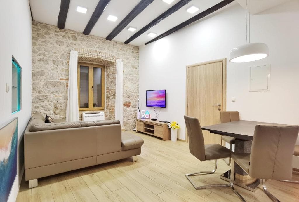 Living and dining area in Design Apartment Y with exposed wooden beams, a stone wall with a window, a sofa and a dining table
