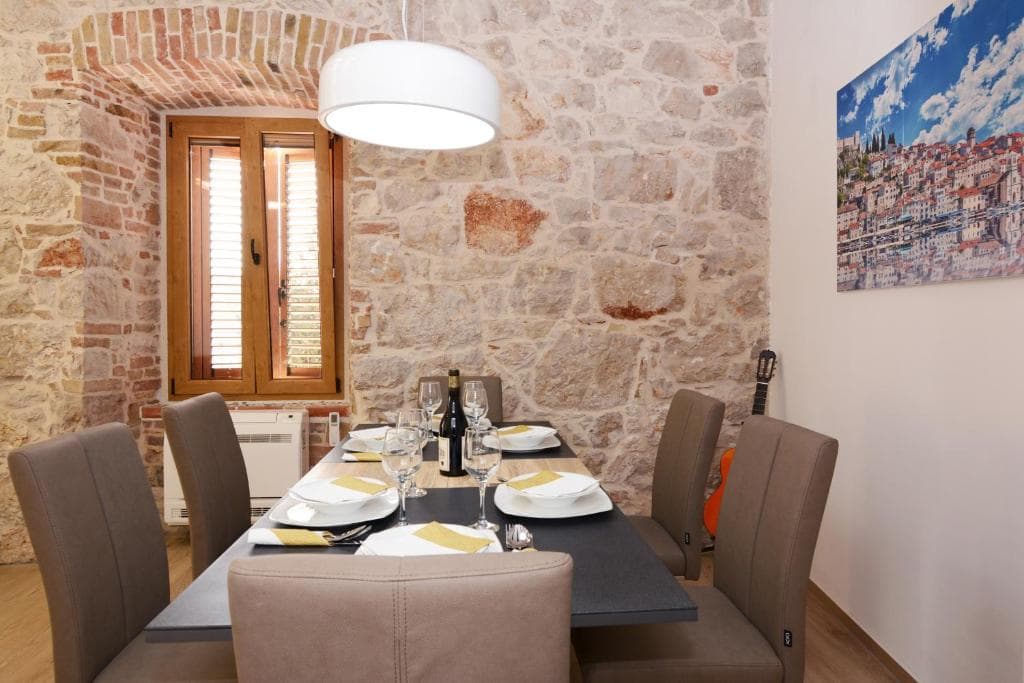 Dining table set in front of an exposed stone wall with a shuttered window
