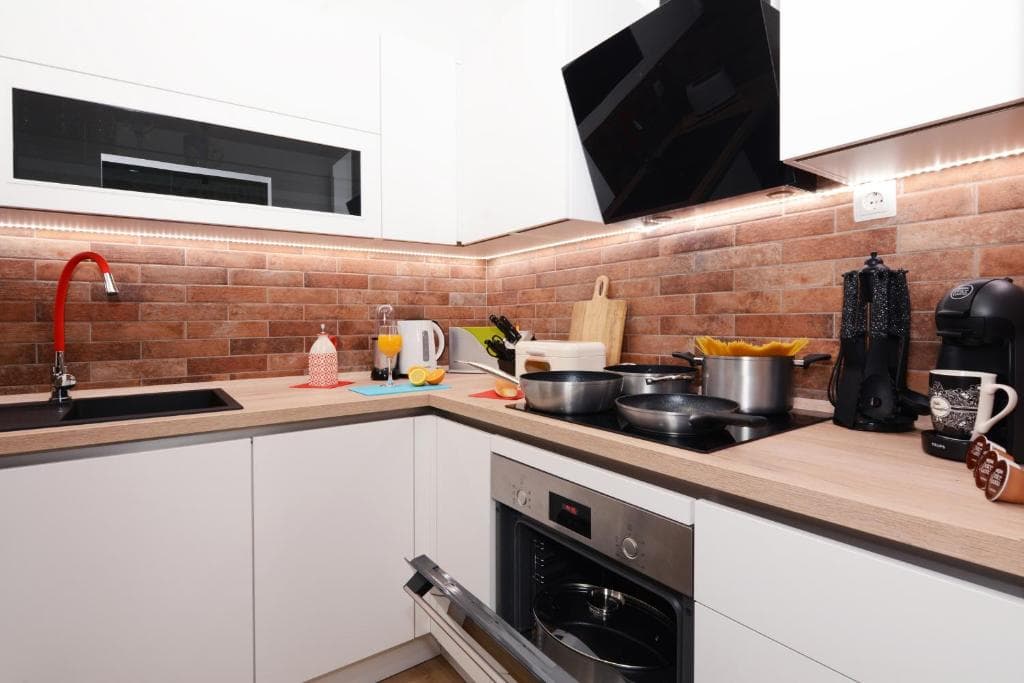 White kitchen with an oven, hob, extractor hood and a brick-style splashback