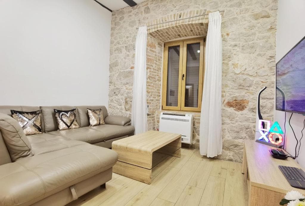 Living room with a beige corner sofa, a coffee table and a stone wall with a curtained window