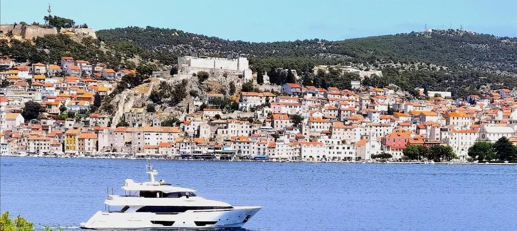 Šibenik seen across the water: the old town on the hillside below a fortress, with a yacht in the channel